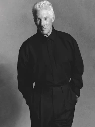 Monochrome portrait of Richard Gere in a black shirt with white hair against a textured grey background.
