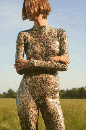 A model poses in a full-body, patterned jumpsuit in a grassy field, under a bright sky, creating a natural and fashionable aesthetic.