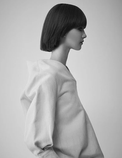 Monochrome side portrait of a young adult female with a short bob haircut and a light-colored garment against a neutral background.