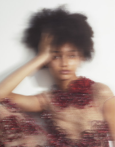 Motion blurred portrait of a woman with dark curly hair touching her head wearing a sheer embellished dress