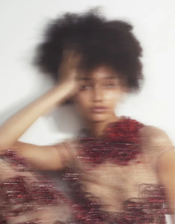 Motion blurred portrait of a woman with dark curly hair touching her head wearing a sheer embellished dress