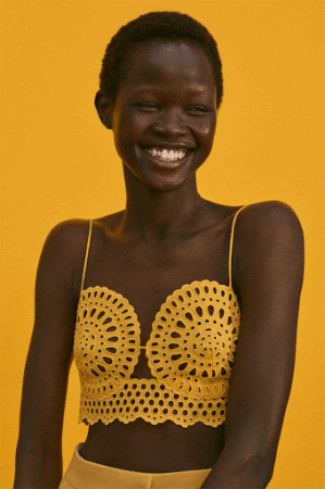 Smiling black woman wearing a yellow eyelet bralette against a solid yellow backdrop