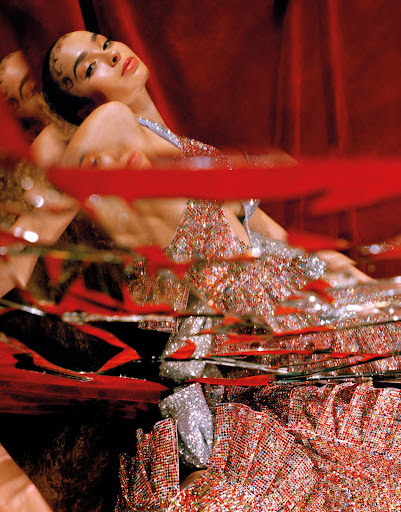 A young woman with dark hair and beaded dress poses against a red curtain, with reflections adding depth to a fashion-forward image.