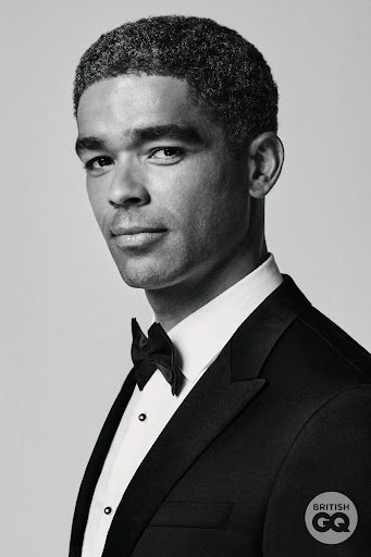 Portrait of a single adult male of African descent wearing a black tuxedo with a bow tie against a white background in black and white.