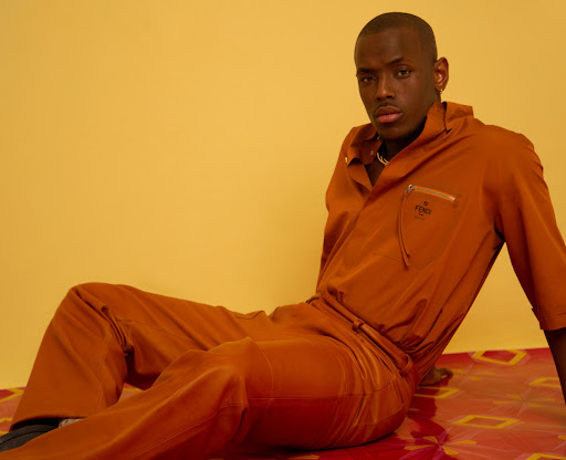 A stylish adult female model poses in a photo studio against a seamless backdrop wearing a tan trench coat and matching heels.