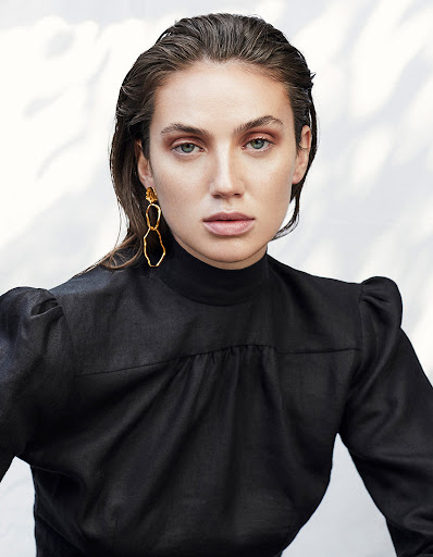 Portrait of a brunette woman wearing gold earrings and a black top in front of a softly textured background. Fashion and beauty shot.