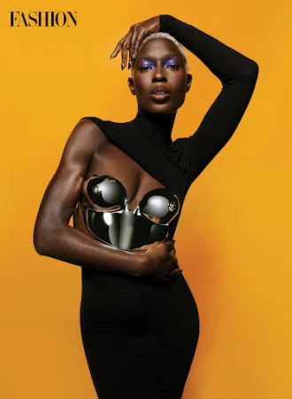 Fashionable dark-skinned woman with platinum hair and silver metallic bra-top poses against yellow background in studio shot.