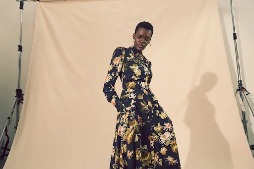 Elegant African-American woman in a floral dress poses in a photo studio, showcasing fashion and style against a neutral backdrop.