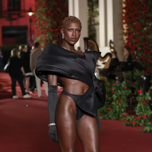 Elegant Black model on the runway in a bold black bikini and striking black satin dress. Red roses and greenery add flair.