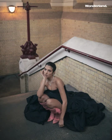 Woman in a black strapless gown and pink boots crouching on stone stairs inside a historic building