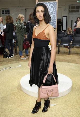 Naomi Scott attends the Chloé Womenswear Fall/Winter 2020/2021 show during Paris Fashion Week, wearing a black skirt and pink purse.