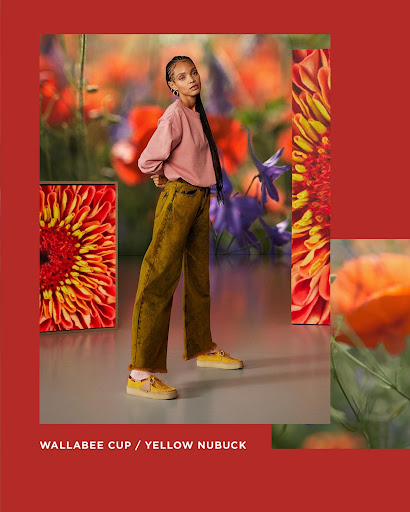 Woman in pink sweater and yellow pants poses with floral art in a studio. Fashion editorial shot with bright colors and modern style.