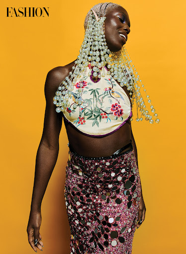 Editorial fashion shot of an African woman wearing a floral halter top and a sequined skirt against a bright yellow background.