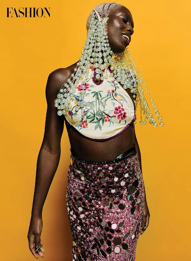 Editorial fashion shot of an African woman wearing a floral halter top and a sequined skirt against a bright yellow background.