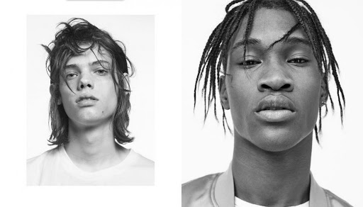 Two adult males in a black-and-white headshot. One with long wavy hair and one with cornrows, both looking directly at the camera.