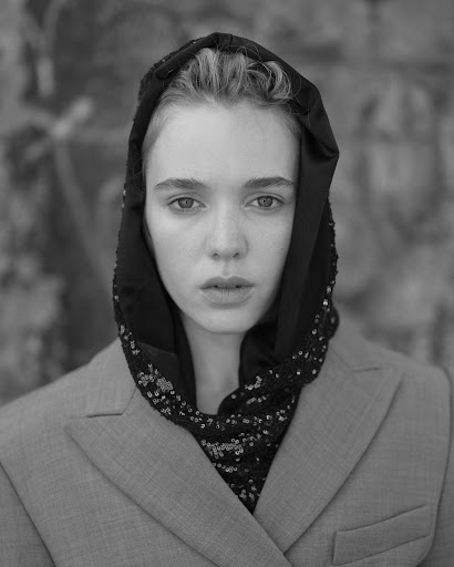 Black and white portrait of a young woman with a hooded sequin shawl, wearing a blazer, with a blurred abstract background.