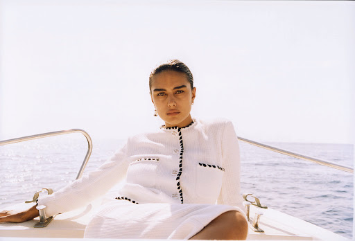 Woman in white textured jacket poses on boat with blue sea background, creating fashion and nautical style imagery.