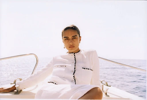 Woman in white textured jacket poses on boat with blue sea background, creating fashion and nautical style imagery.