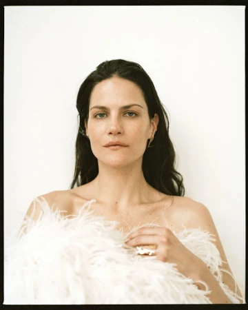 Portrait of a woman with long dark hair wearing a white feather garment against a plain white background