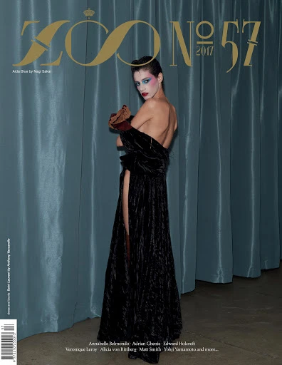 Magazine cover featuring a fashion model in a black dress with blue eye shadow in front of a blue curtain backdrop.