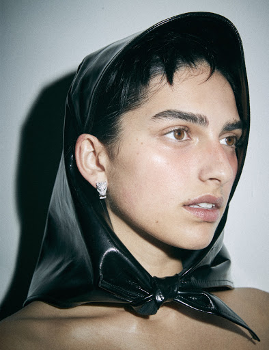 Close-up portrait of a young adult woman with dark hair wearing a black hood, set against a neutral background. Emphasizing her facial features.