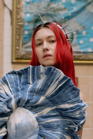 Close-up portrait of a woman with red hair wearing a spiked tiara and blue and white pleated ruff collar.