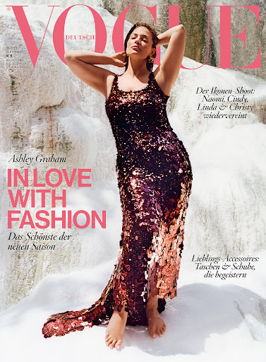 Ashley Graham poses in a sequined dress for a Vogue Deutsch cover against a textured white rock formation, bathed in bright sunlight.