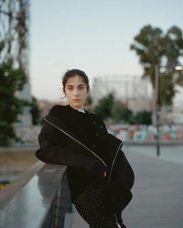 Woman in a black jacket leaning on a railing outdoors during twilight by photographer Marco Braca.