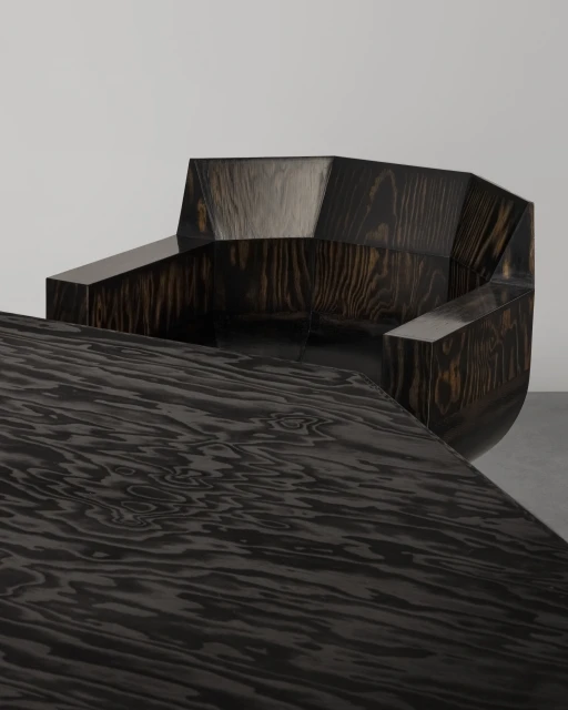 Geometric wood chair and table set with dark, swirling grain, highlighted by bright studio lighting against a light gray backdrop.