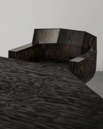 Sculptural dark stained wood armchair with a faceted backrest positioned behind a matching wooden table.