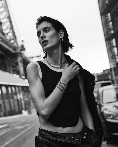 Black and white portrait of a woman with wet look hair wearing a dark tank top and bracelets on a city street
