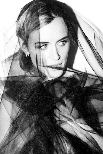 Black and white portrait of a woman partially veiled with black tulle, close up, with stark lighting and shadow, in studio.