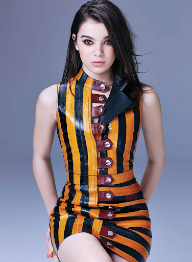 Striking portrait of a woman with smokey eyes wearing a bold, vertically striped, orange-and-black mini dress against a gray background.