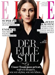 Close-up portrait of Olivia Palermo wearing a dark sleeveless collared coat with a thin black belt on a white background