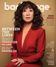 Portrait of Sandra Oh with curly dark hair wearing a red wrap dress against a warm beige studio backdrop with magazine cover text.