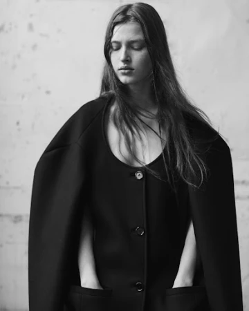 Portrait of a female model with dark long hair wearing a black buttoned coat draped over her shoulders in Paris