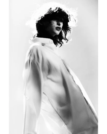Monochrome portrait of an adult female with dark hair and red lipstick, wearing a white blouse, in a photo studio environment.