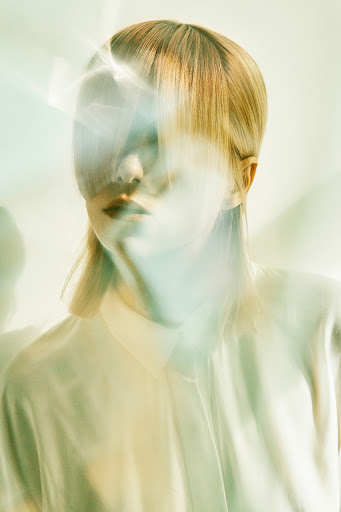 Portrait of a fair-skinned woman with blonde hair and a white shirt. Light flares and blurs create a dreamy, ethereal aesthetic.