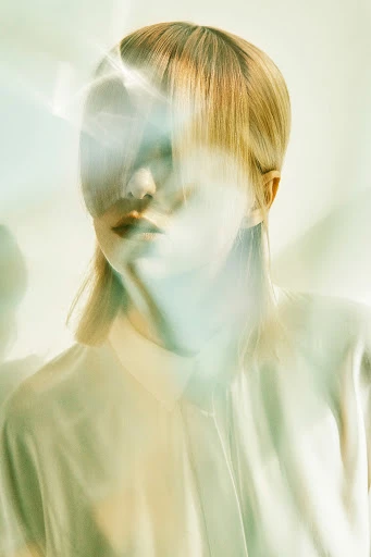 Portrait of a fair-skinned woman with blonde hair and a white shirt. Light flares and blurs create a dreamy, ethereal aesthetic.