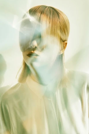 Portrait of a fair-skinned woman with blonde hair and a white shirt. Light flares and blurs create a dreamy, ethereal aesthetic.