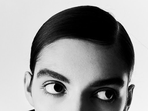 Black and white portrait of a woman with slicked back dark hair, her face close to the camera, her eyes glancing to the side.