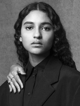 Monochrome portrait of a woman with dark wavy hair wearing a structured blazer, with a hand resting on her shoulder.