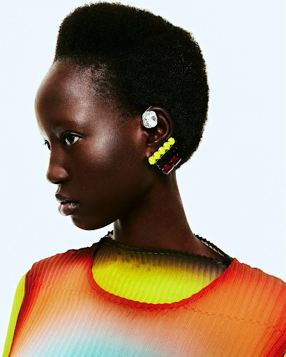 Close-up of a Black woman wearing colorful clothing and unique statement earrings on a white background in a beauty fashion editorial.