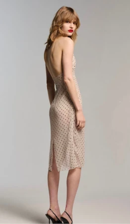 Model wearing a strapless polka dot midi dress and black heeled sandals standing against a plain light grey studio background.