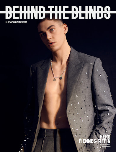 Fashion magazine cover featuring a bare-chested man in an embellished suit, jewelry, against a dark background, showcasing menswear fashion.