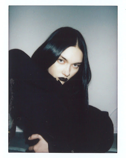 Portrait of a woman with dark hair and black lipstick sitting indoors by Quentin Guyen.