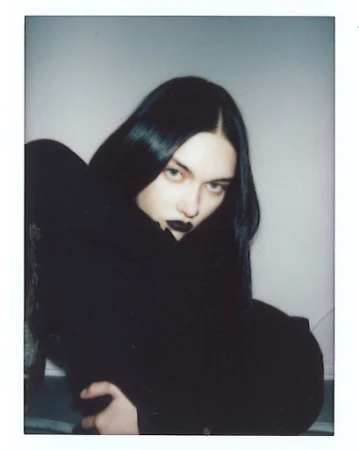 Portrait of a woman with dark hair and black lipstick sitting indoors by Quentin Guyen.
