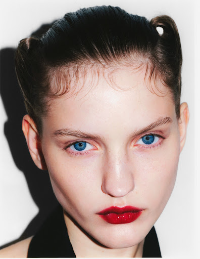 Close-up portrait of a young woman with a bold red lip and stylized hair on a bright white background, showcasing beauty and fashion.
