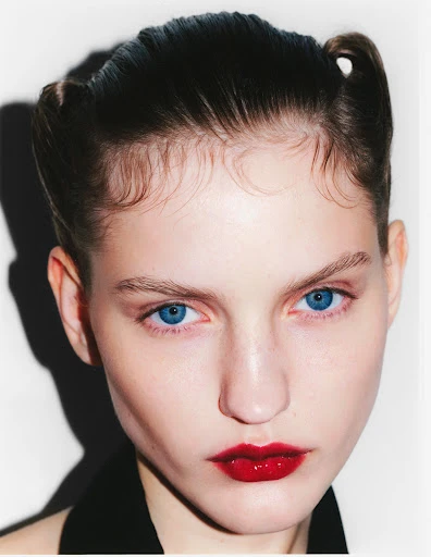 Close-up portrait of a young woman with a bold red lip and stylized hair on a bright white background, showcasing beauty and fashion.