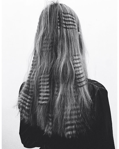 Back view of a woman with long, gray, wavy hair styled with patterned hair clips, set against a plain white studio backdrop.